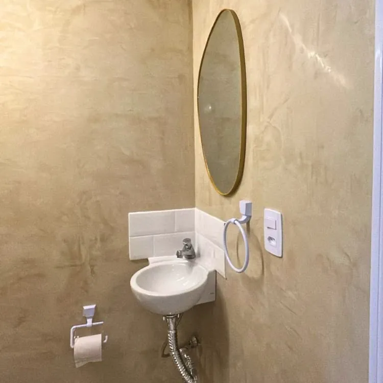Banheiro com parede em acabamento decorativo bege de efeito marmorizado, serviço da Alpha Empreiteira