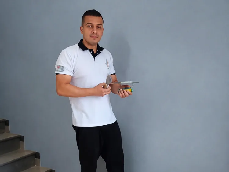 Rodrigo, responsável técnico da Alpha Empreiteira, segurando espátula e ferramentas de pintura ao lado de parede pintada
